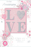 Displayed as if propped on a mantel in an Eastcote living room, this anniversary card radiates a soft, lingering romance through its harmonious blend of pastel pinks, off-whites, and silvery grey highlights. The focal point is the word LOVE, set in large, raised letters that are generously edged with fine glitter, giving them a refined sparkle and a touchable texture reminiscent of the crystal-sugar sheen on delicate petals. These letters rest against a blush pink panel, its surface smooth yet glowing gently, as though catching the mild daylight that often bathes local homes near Eastcote's parks. Around this central word, a dance of illustrated flowers and leaves sweeps across the card in graceful curves, like the natural arc of stems in a hand-tied anniversary arrangement. The blossoms, drawn with slender, confident lines and soft shading in hues of blush, ivory, and silvery taupe, appear to open slowly, suggesting the unfolding of shared years and quiet moments. Slender vines and tiny curled tendrils thread between the blooms, creating a sense of light movement, while small hints of glitter and silver foil nestled in the design add a whisper of celebration rather than a loud sparkle. The background blush gently gradients outwards, providing a soothing, almost dreamlike aura that wraps the design in warmth. Near the base or to one side, scripted words in elegant, flowing calligraphy convey loving anniversary wishes, their inked curves mirroring the floral swirls around them. The composition feels poised and intimate, much like an anniversary bouquet delivered across Eastcote: thoughtfully designed to honour enduring affection, shared memories, and the quiet joy of a love that continues to blossom.
